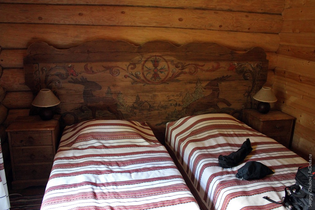 Кровати в номере. Вся мебель искусственно состарена. Над кроватью сделана панель, которая напоминает домовую роспись наших деревень.